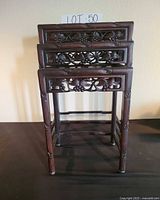 Front view of three stacked carved hardwood nesting tables showing pierced aprons and faux bamboo legs