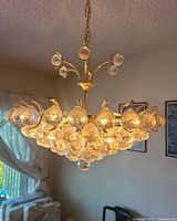 Chandelier lit, side view showing brass frame, central rod, chain, and crystal drops