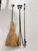 Full view of three fireplace tools laid out: broom, poker, coal rake