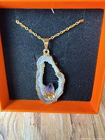 Front view of agate geode pendant with amethyst point on chain in box