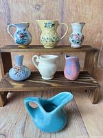 All seven ceramic miniature pitchers and bud vases displayed on wooden stand