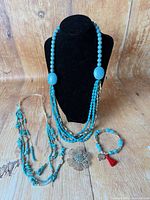 Overview showing three necklaces on bust and surface, bracelet and brooch