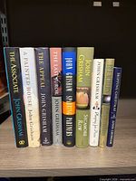 Front view of nine John Grisham hardcovers standing upright on shelf showing spines