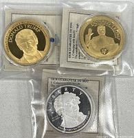All three commemorative coins in plastic sleeves, two gold-tone Donald Trump coins and one silver dollar
