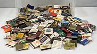 Overview of entire mound of matchbooks and matchboxes in clear storage bin