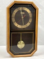 Full view of wall clock showing wood-grain case and pendulum