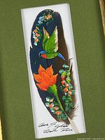 Close-up of painted feather showing hummingbird and flower detail with artist signature
