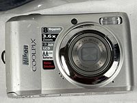 Front view of Nikon Coolpix L19 camera showing lens and feature labels (8MP, 3.6× zoom, 2.7-inch LCD).