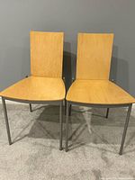 Front view of two IKEA Assar chairs showing wood veneer seats/backs and grey metal legs