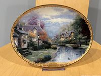 Front view of oval collector plate displaying Lamplight Brooke artwork with gold border