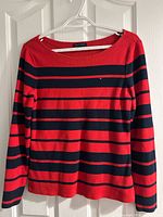 Front view of red and navy striped Tommy Hilfiger knit top hanging on hanger