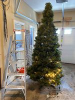 Full view of assembled tree beside ladder; some lights on lower section lit