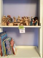 Shelf showing corn husk figurines on upper shelf and row of books below