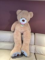 Full view of giant light tan teddy bear sitting on sofa