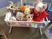 Rocking doll bassinet with pink fabric sling holding seven assorted plush toys