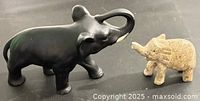 Side view of black ceramic elephant and tan stone elephant