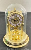Front view of brass-tone anniversary clock under glass dome