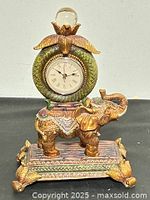 Front view of resin elephant mantel clock showing dial, ornate base, birds, and glass sphere