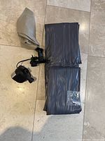 Folded grey/black inflatable mattress with pump and small accessory bag on tile floor