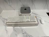 Mac mini, keyboard on box, mouse visible on countertop