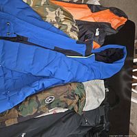 Overview of blue jacket, camo jacket, orange/charcoal jacket and snow pants