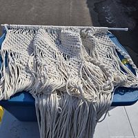 Full macramé hanging draped over bin showing pattern, fringe and tension rod