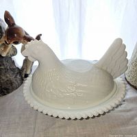 Milk glass hen dish with nearby ceramic fawn vase and portion of pottery vase visible