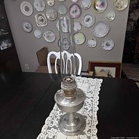 Full view of pewter Aladdin oil lamp with chimney on table