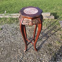 Full view of carved wooden plant stand with marble inset top outdoors