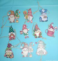 Overview of all ten flat gnome ornaments with jute hangers on blue background