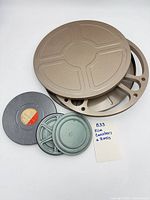 Group shot of tan 16mm reel and lid, grey 16mm canister, two green 8mm canisters