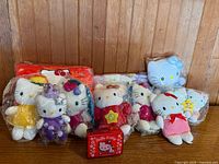 Group shot showing six wrapped Hello Kitty plush dolls and red mini case