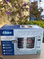 Factory sealed box showing Oster Digital French Door Oven with Convection front panel and specs