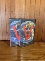 Front view of both VHS cases showing Earth artwork and red V