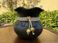 Front view of black textured pot showing scalloped rim, rope band and hanging beads