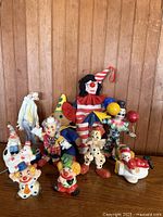 Group shot of 13 assorted clown figurines on wooden surface