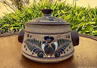 Front view of lidded pot showing floral decoration and one side handle