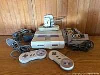 Overall lot with console, controllers, power adapter, RF cable, rabbit-ear antenna resting on console, game cartridges stacked