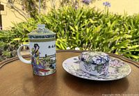 Mug with lid beside floral plate and covered dish displayed on table