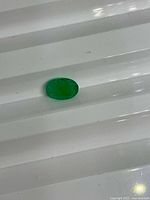 Oval green emerald on ridged white surface