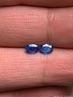 Two blue oval sapphires on fingertip, face-up view
