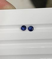 Two round blue sapphires on white tray, showing faceting and colour