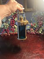 Full view of brass lantern held by handle showing blue glass lens