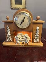 Front view showing clock face, wood case, metal appliqués, fireplace insert