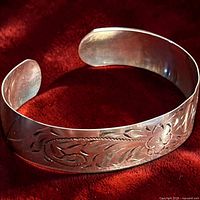 Angled view of etched sterling silver cuff bracelet on red background