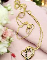 Necklace laid out showing gold-tone box chain, lobster clasp, heart pendant with sapphire stones