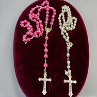 Both rosaries displayed on burgundy oval stand