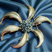 Front view showing gold-tone petals and blue rhinestone center