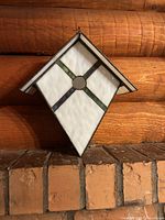 Front view of stained glass birdhouse hanging against wood wall