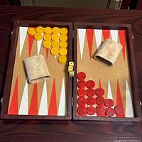 Open backgammon board showing yellow and red Bakelite checkers, dice, and cups